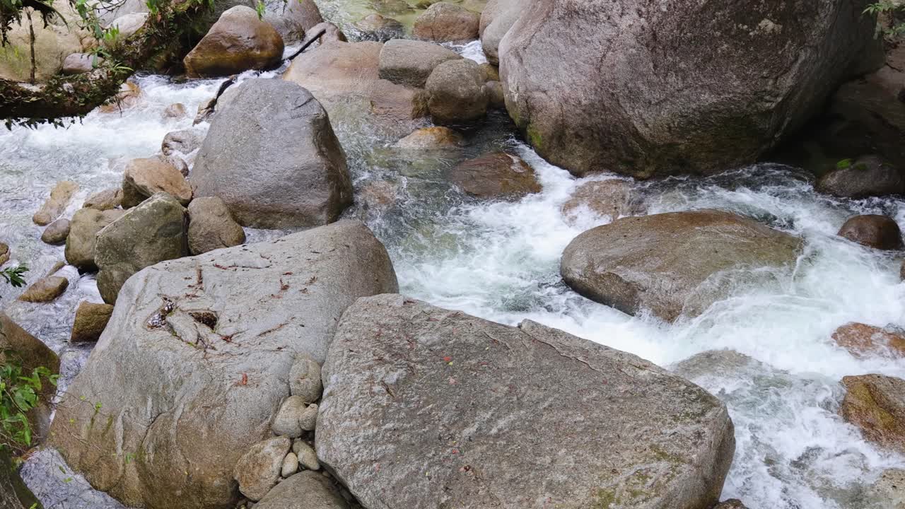 Clear water rushes over large boulders in Mossman Gorge, surrounded by lush greenery and natural light