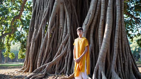 young man wearing traditional indian clothing standing with closed eyes near a banyan tree in a park, embracing spirituality and cultural heritage
