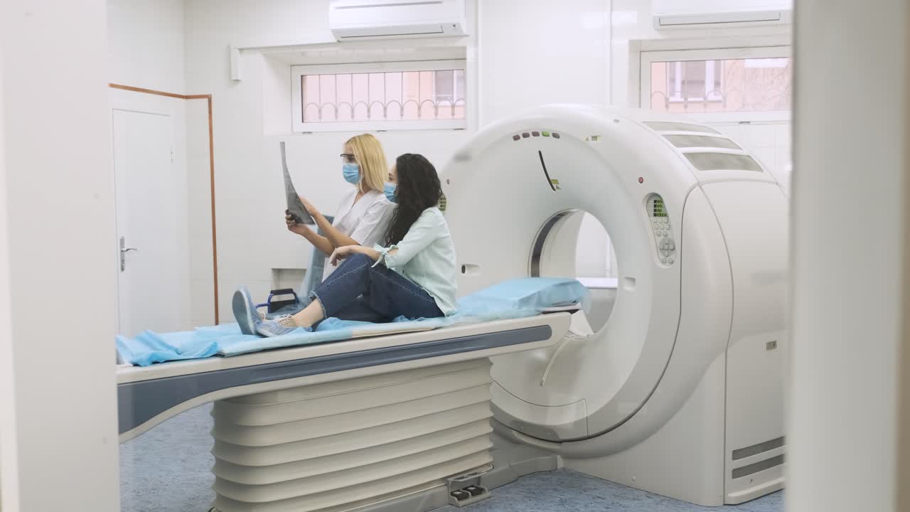 la radióloga explica los resultados de la tomografía computarizada para una paciente joven, mostrando la instantánea con imágenes, observando y analizando la tomografía computada en una clínica moderna junto a un escáner computarizado moderno