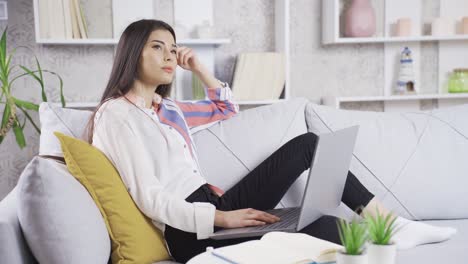 Nachdenkliche-Junge-Frau-Sitzt-Zu-Hause-Auf-Dem-Sofa-Und-Schaut-Auf-Ihren-Laptop.