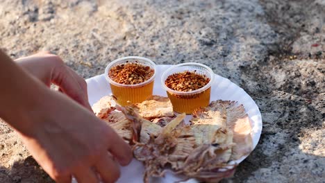 hands preparing grilled squid with spicy sauce