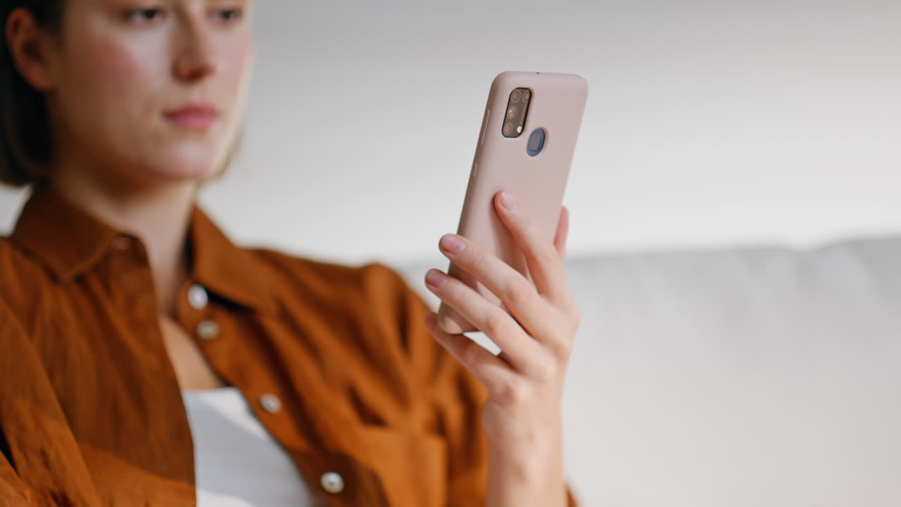 Lady watching social media on cellphone sitting calmly at home sofa closeup