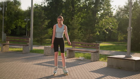 joven patinando al aire libre en el parque, rodeada de vegetación, bancos y postes de lámpara con sombras proyectadas en el camino pavimentado, con lienzo blanco debajo del banco