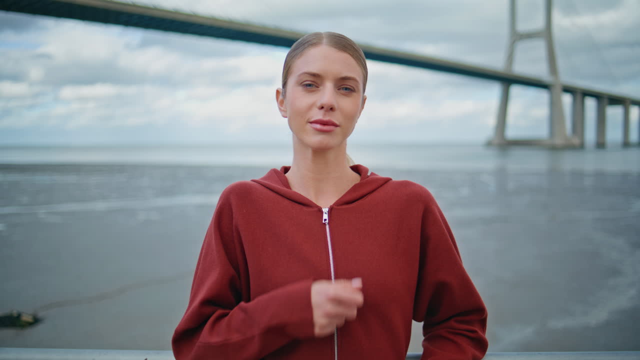 Attractive athlete resting city bridge view. Relaxed woman zipping sportswear