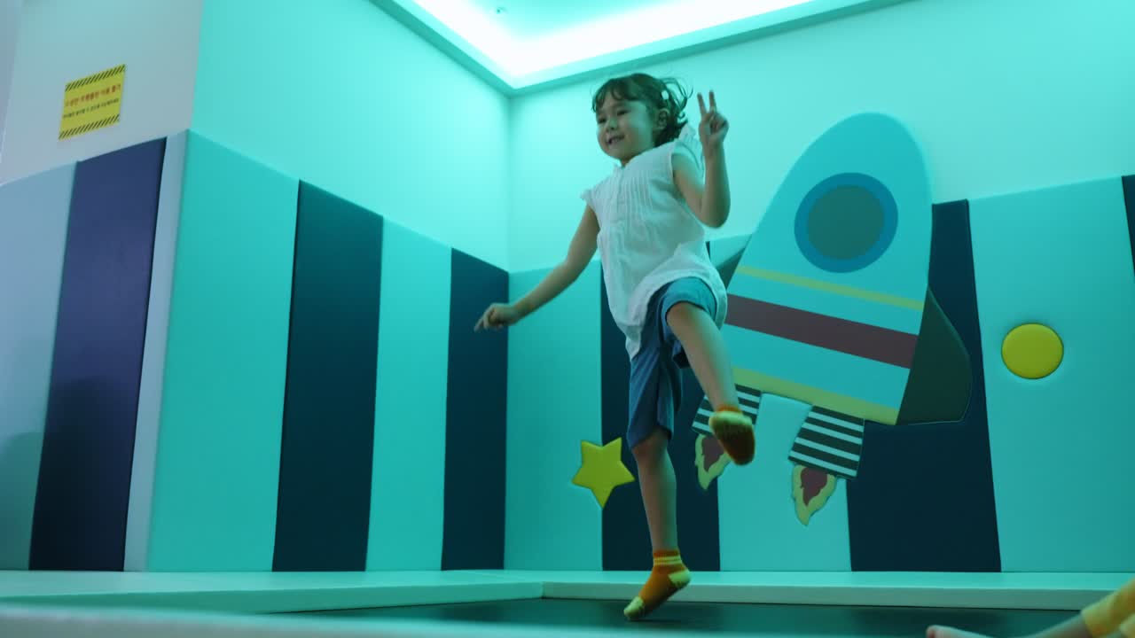 An excited five-year-old girl with pure joy on her face jumps high on a trampoline in a playroom, captured in a beautiful slow-motion shot showing her happiness and energy
