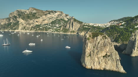 Toma-Panorámica-Con-Drones-De-Grandes-Yates-De-Vela-Anclados-En-Capri-Rock-En-Un-Día-Soleado