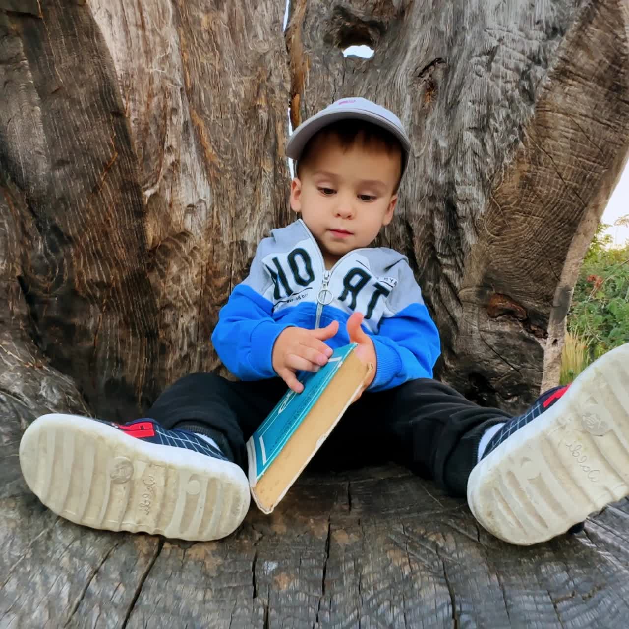 Un niño pequeño se sienta en la estatua tallada en madera. El bebé sostiene el libro con las manos y mira a su alrededor.