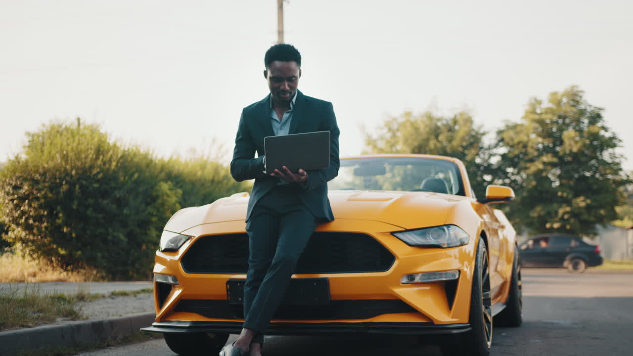 hombre de negocios trabajando en una computadora portátil al lado de un coche convertible amarillo