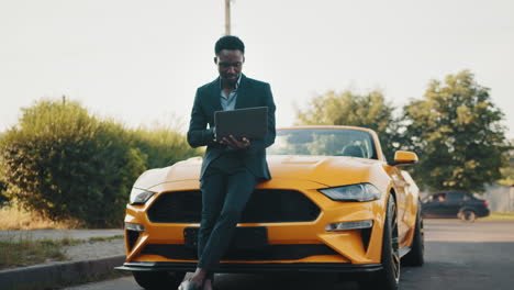 businessman working on a laptop next to a yellow convertible car