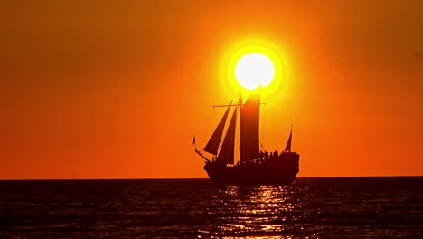 a beautiful slow-motion shot shows the silhouette of a vintage tall ship with tourists sailing peacefully across the baltic sea as the sun sets on the horizon, creating a golden glow