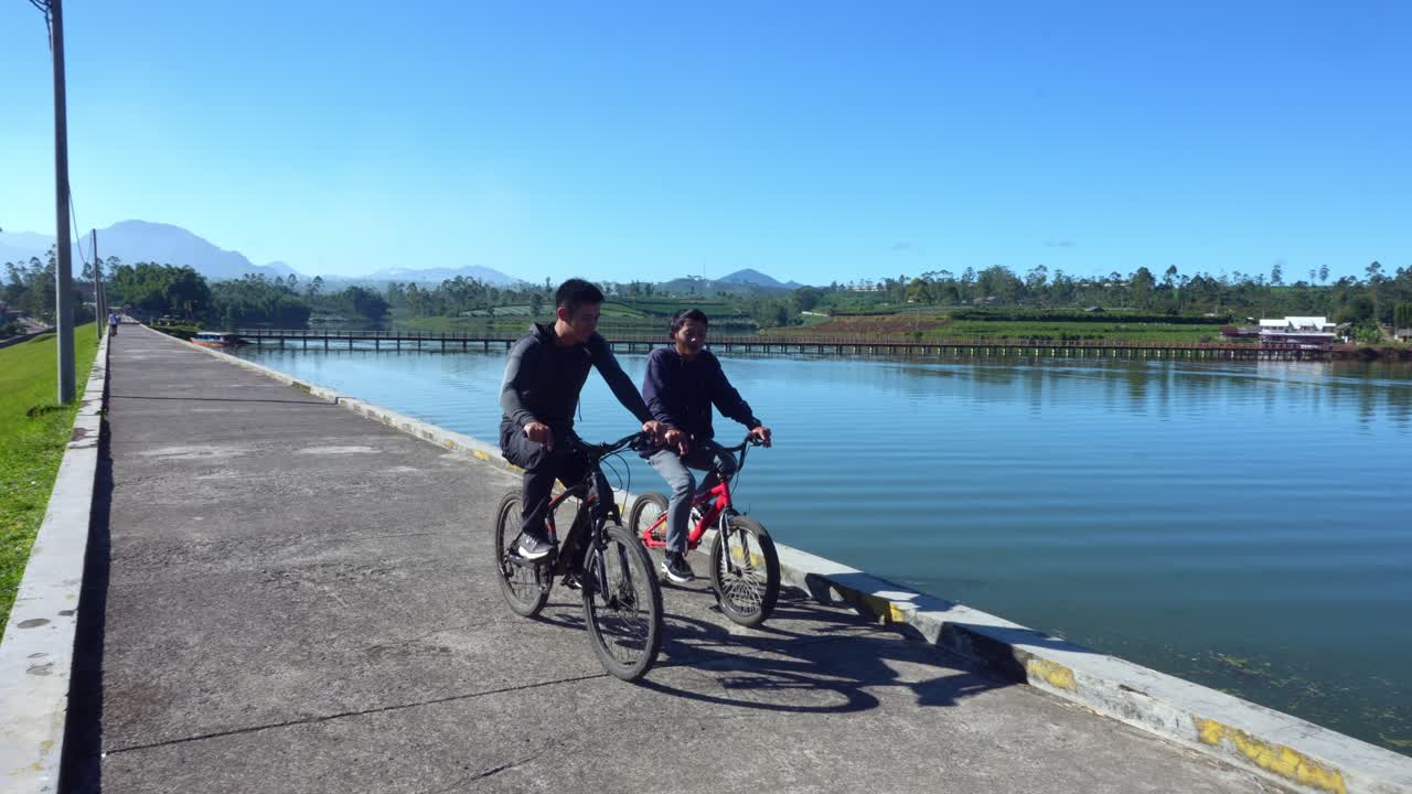 Friends Biking Beside Calm Lake, Smiling And Chatting During Scenic Countryside Ride