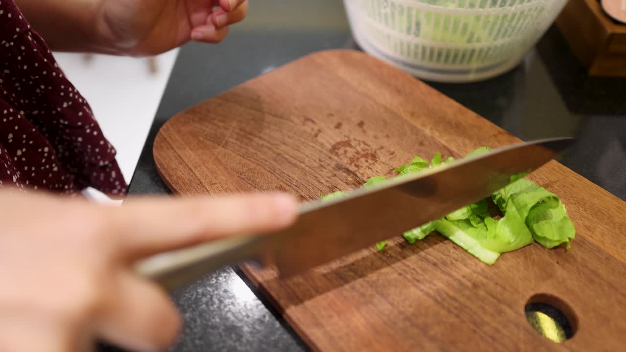 Et nærbilde viser en kokk som hakker grønn salat med en kniv på et trefjøl.