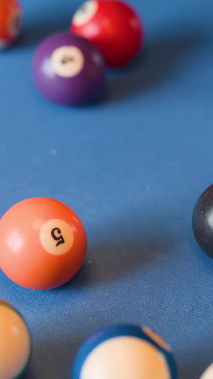 Colorful billiard balls scatter across blue felt table, shallow depth of field, natural lighting