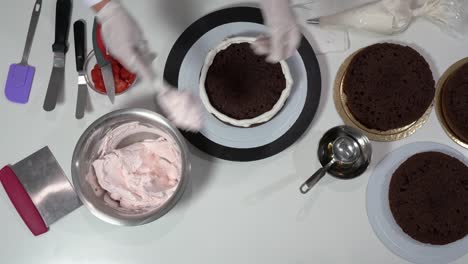 front shot of a baker using an icing spatula to carefully touch up sides of cream covered cake.