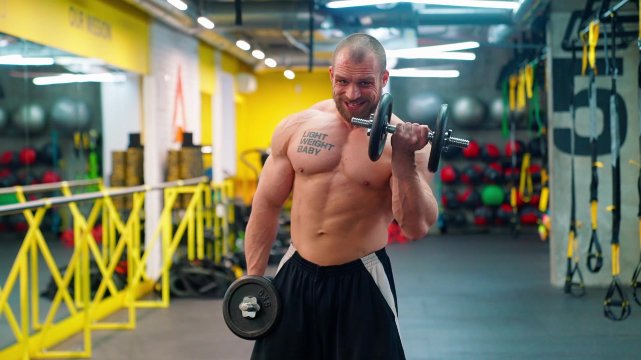 Uomo forte e muscoloso che esegue un curl bicipiti con manubri in palestra.