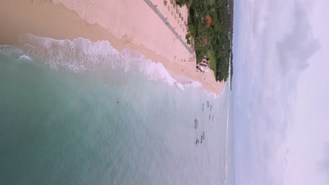 vertical drone shot of waves rooling from the clear blue sea on geger beach in bali