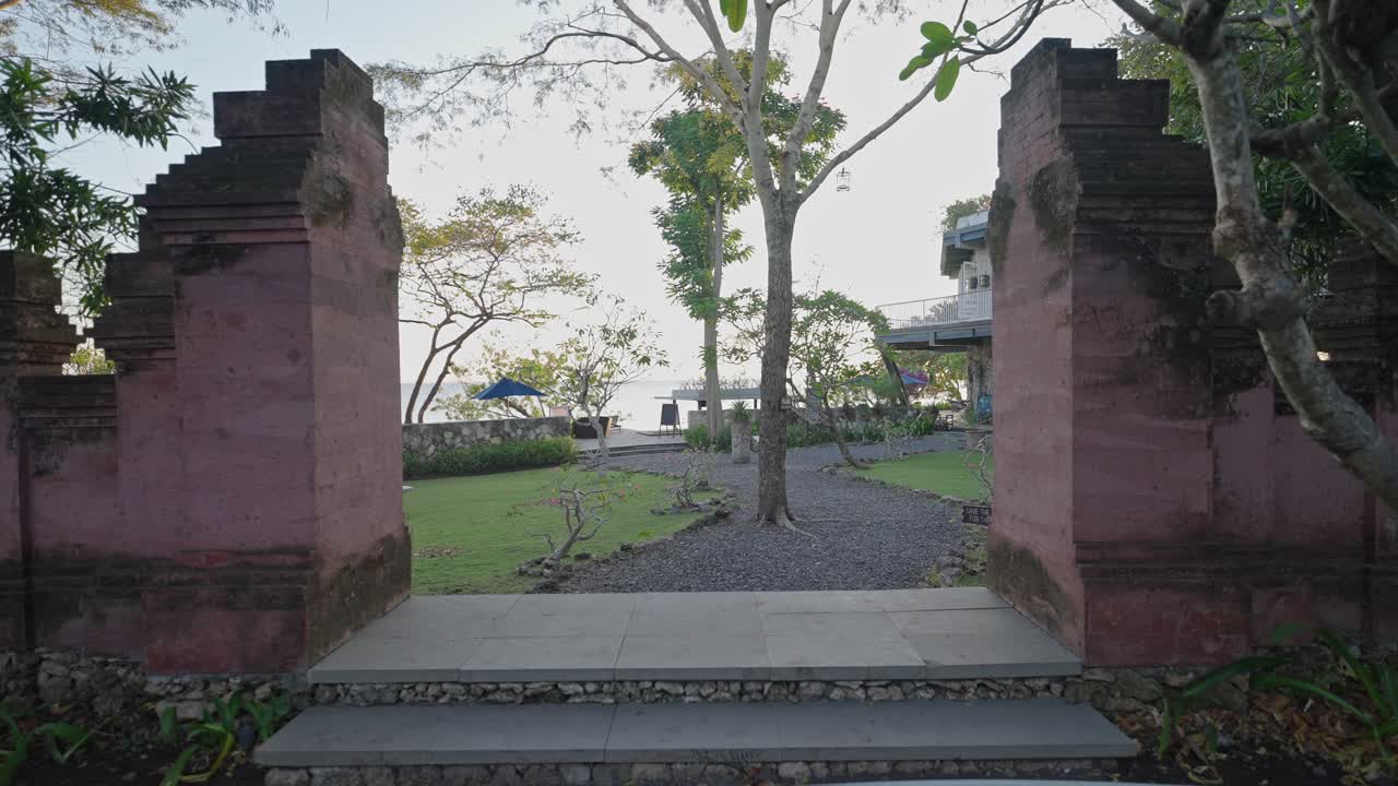 Gerakan maju yang mulus menggunakan penstabil gimbal melewati gerbang tradisional Bali. Pemandangan sinematik lebar menyoroti arsitektur budaya, simetri, dan suasana perjalanan yang imersif di Bali.