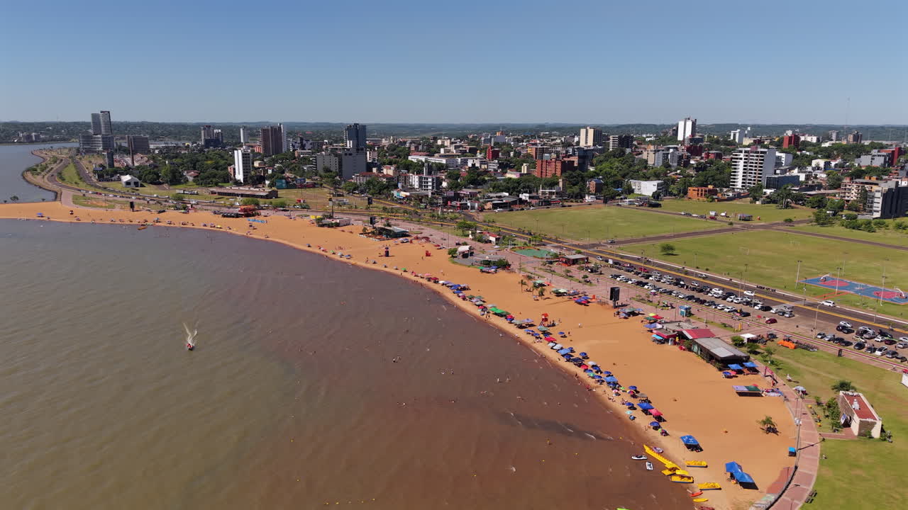 Enjoy an establishing aerial view of Encarnacion, Paraguay, highlighting the golden beaches and vibrant city skyline at Playa San Jose.
