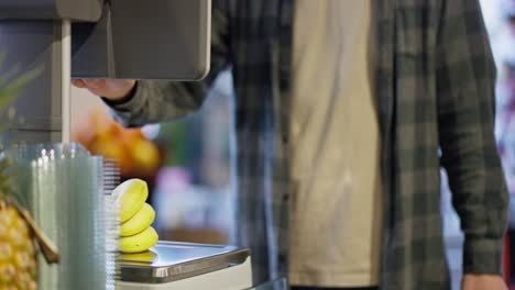 Close-up-Supermarket-visitor-weighs-bananas-using-scales-in-supermarket.-A-guy-in-a-plaid-shirt-uses-a-scale-to-weigh-bananas-while-shopping-in-a-supermarket