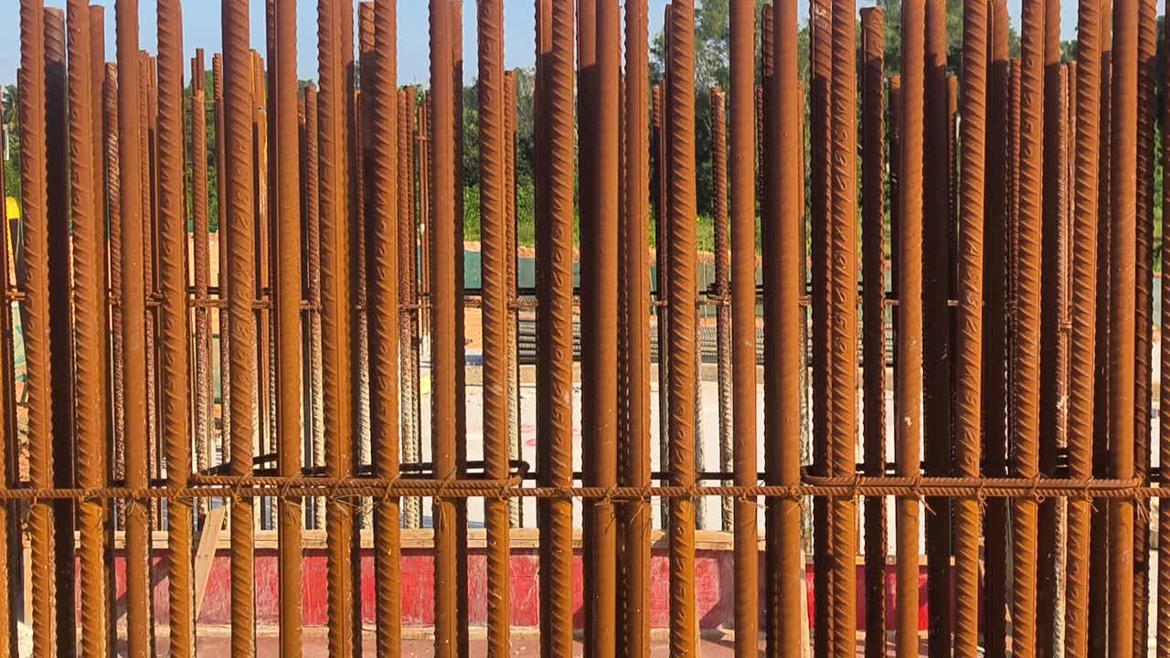 Vertical reinforcement bars show visible surface rust at a construction site. The steel rods must be cleaned thoroughly before concrete pouring begins. Proper maintenance ensures structural integrity
