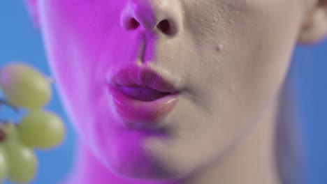 close up of woman's face and mouth, eating and chewing green grapes, colorful studio shot