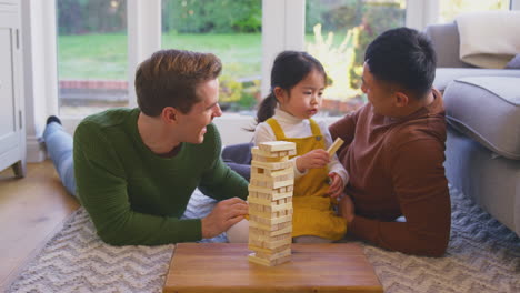 Familia-Con-Dos-Padres-Jugando-Con-Su-Hija-En-Casa-Apilando-Ladrillos-De-Madera-En-La-Torre