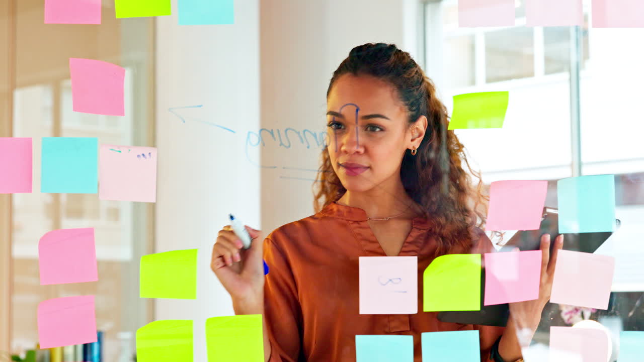 una diseñadora planea ideas en una pared de vidrio