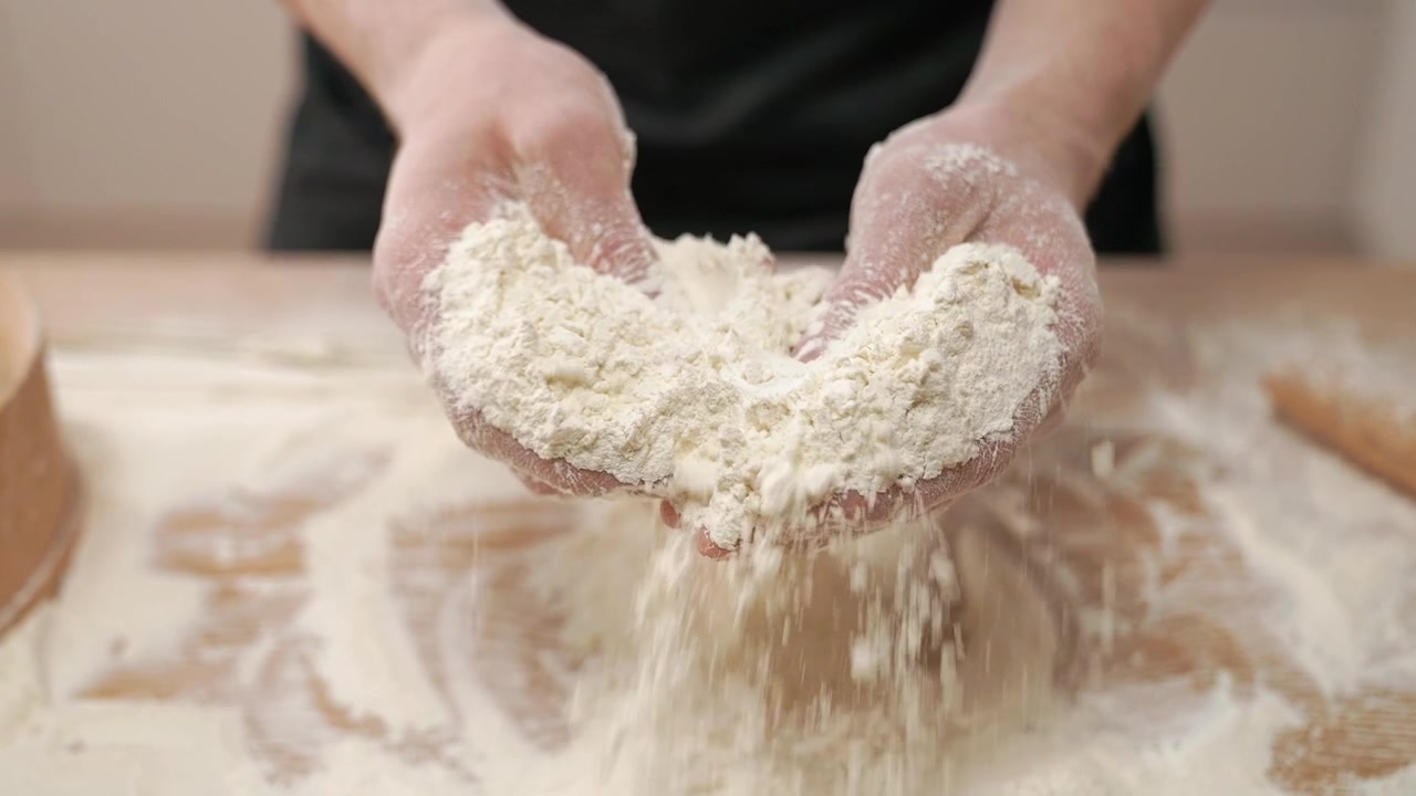 Mani che setacciano farina bianca su un tavolo di legno al rallentatore