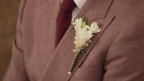 close-up of the groom's pink suit, adorned with a white floral boutonniere and a dark red tie