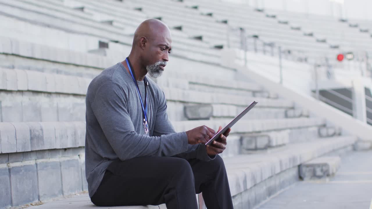 African american male coach sitting, time checking and making notes