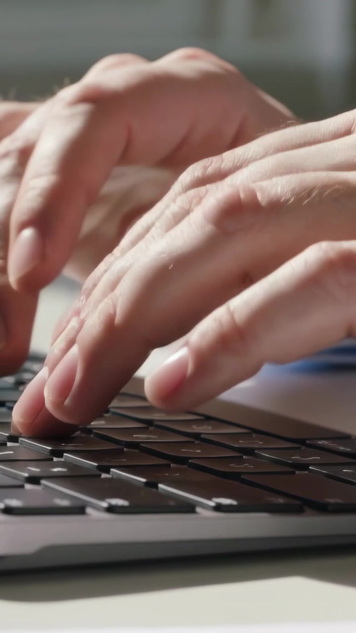 Video verticale: Mani che digitano, passando da una posizione di riposo a premere i tasti su una scrivania vicino alla finestra, con tasti neri.