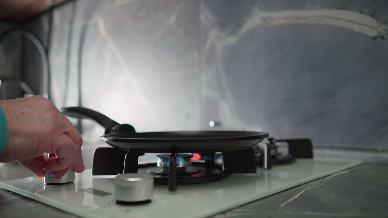 Close-up of elderly woman s hand adjusting gas stove burner. Modern kitchen setting with sleek design. Focus on cooking preparation and domestic environment with soft lighting
