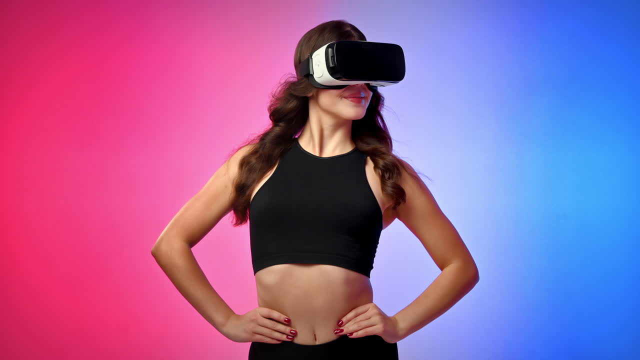 Young smiling woman in a tracksuit in virtual reality VR headset looking around in a studio with blue and red background