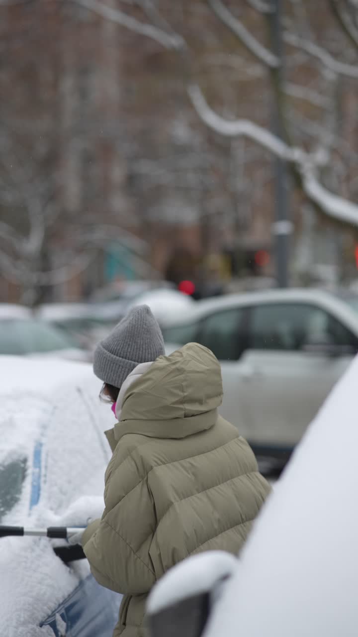 mujer limpiando la nieve del parabrisas del coche en invierno