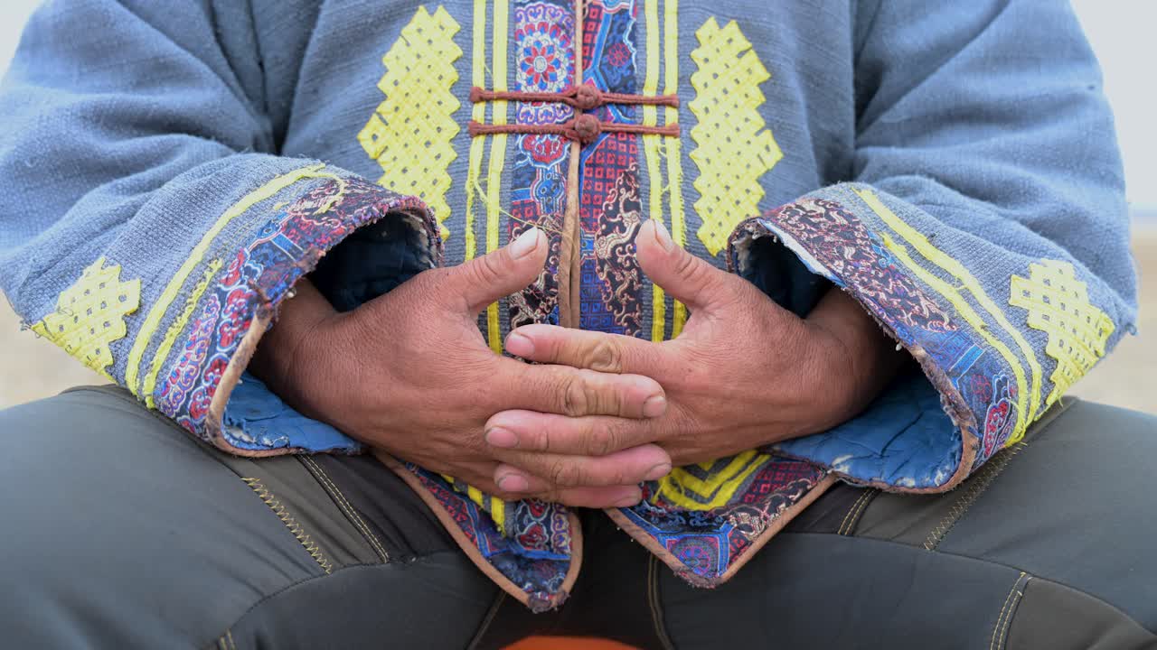A close-up on the weathered hands of a nomad man as he talks. His expressive gestures highlight the intricate details of his traditional Mongolian deel