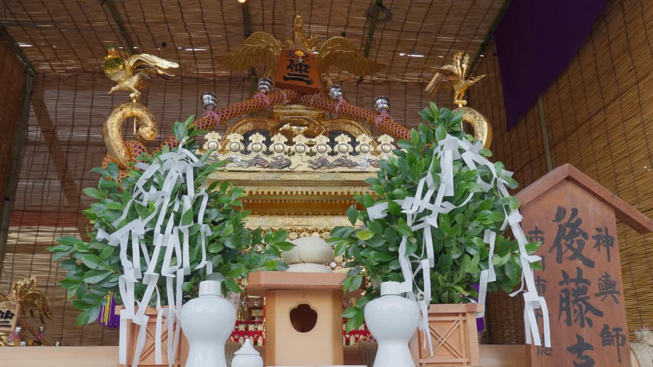 A close-up of the front of a decorated Japanese mikoshi, with ceremonial greenery and paper streamers