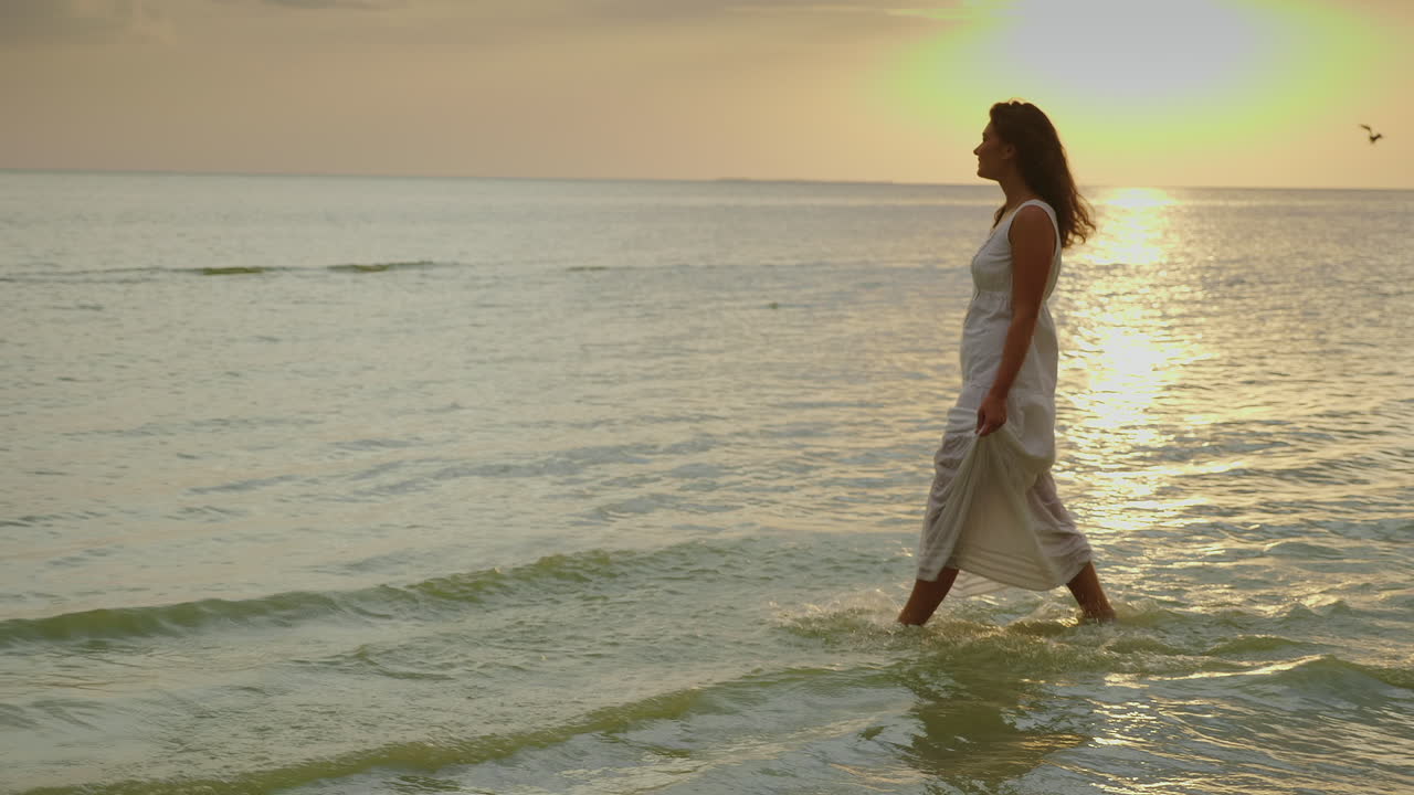 가벼운 여름 드레스를 입은 젊은 여성이 배경을 배경으로 물가를 따라 걷고 있다