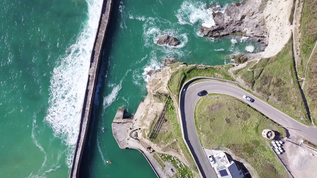 автомобили едут по холму маяка по кривой дороге с океанскими волнами на пирсе возле деревни portreath, корнуолл, англия летом