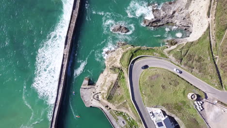 cars driving in lighthouse hill by curve road with ocean waves on pier near village of portreath, cornwall, england in summer