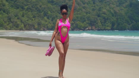 beautiful black woman in pink swimsuit posing on tropical beach