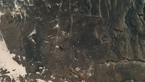 Close-up-Aerial-footage-looking-down-as-waves-crash-on-bedrock-on-the-beach