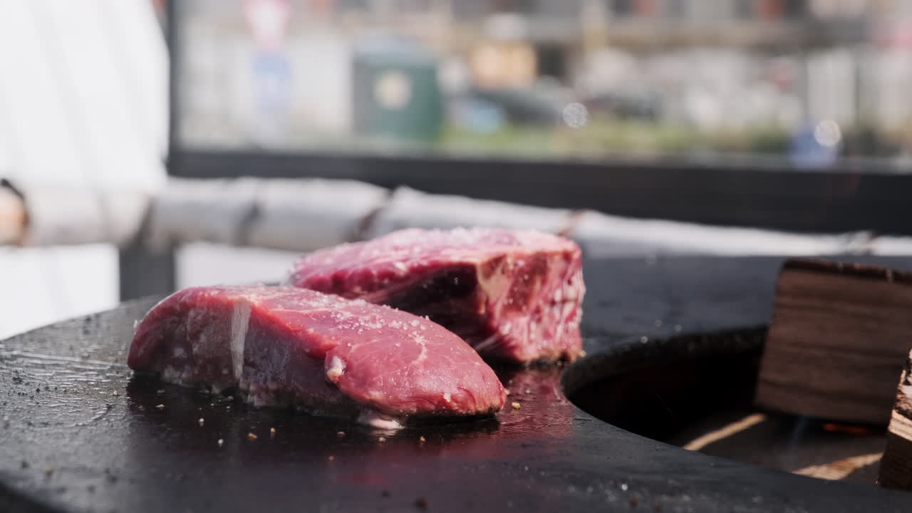 Raw beef steak sizzling on a hot outdoor grill. Two seasoned raw beef steaks cooking on a hot plancha grill with open flames and smoke