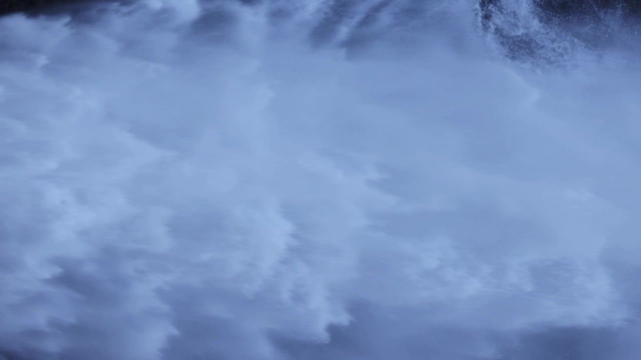 Roaring torrents of whitewater surge out of a hydroelectric dam in Portugal. The wide shot captures forceful motion, mist, and turbulent flow in bright daylight. No people are visible.