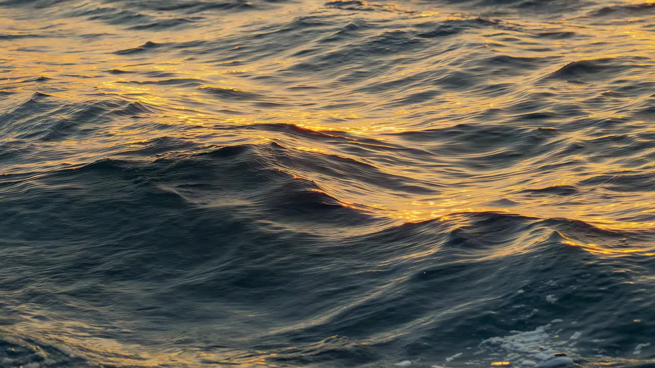 Sich verschiebendes Sonnenlicht, das das offene Meer antreibt, reflektiert goldene Schimmer und bildet weißen Schaum bei Sonnenuntergang