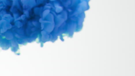 defocused shot of blue paint or dye dropped into water against white background to create swirling colourful smoke background