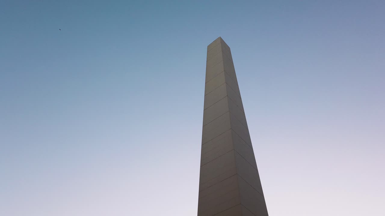 The Buenos Aires Obelisk at sunset on 9 de Julio Avenue, iconic landmark and urban symbol, establishing tilt up against blue sky