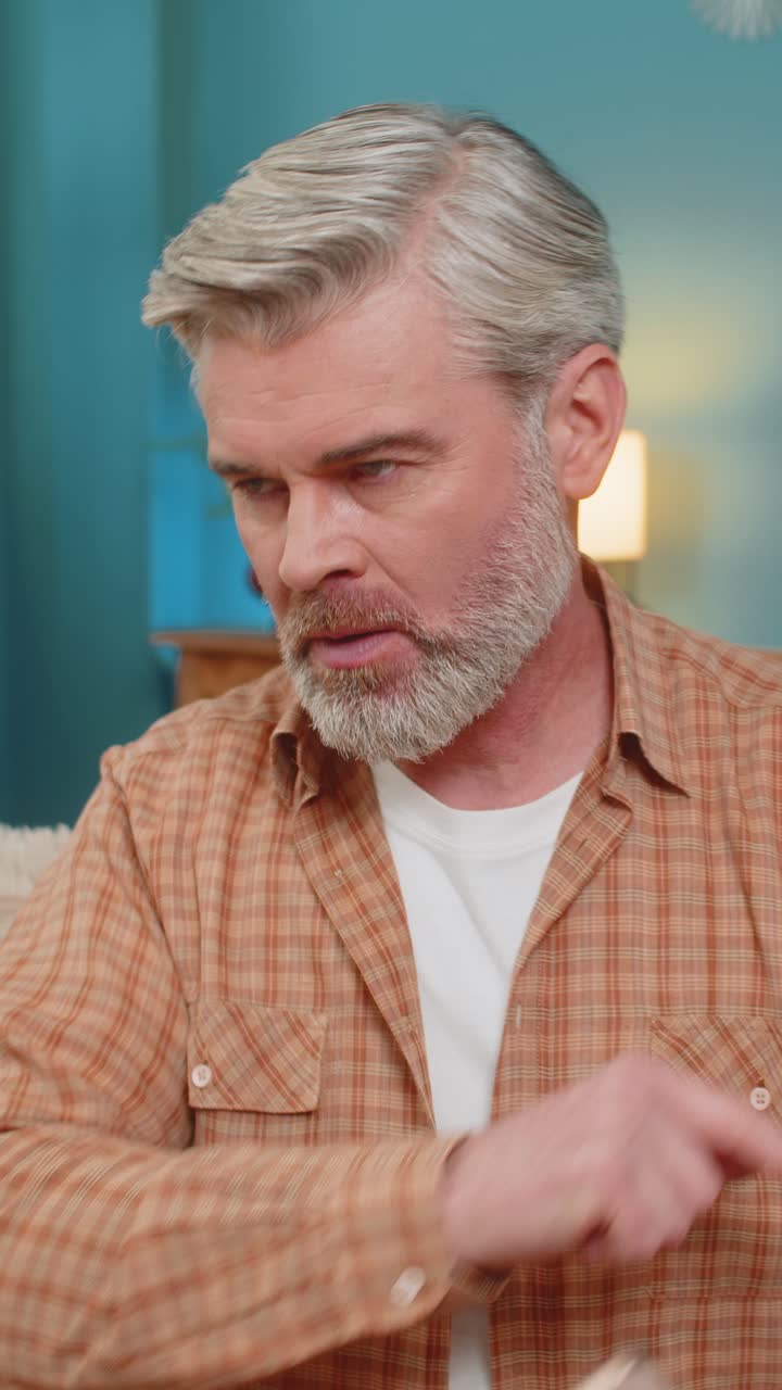 Mature man having phone argument on speaker expressing stress and negative emotions on sofa at home