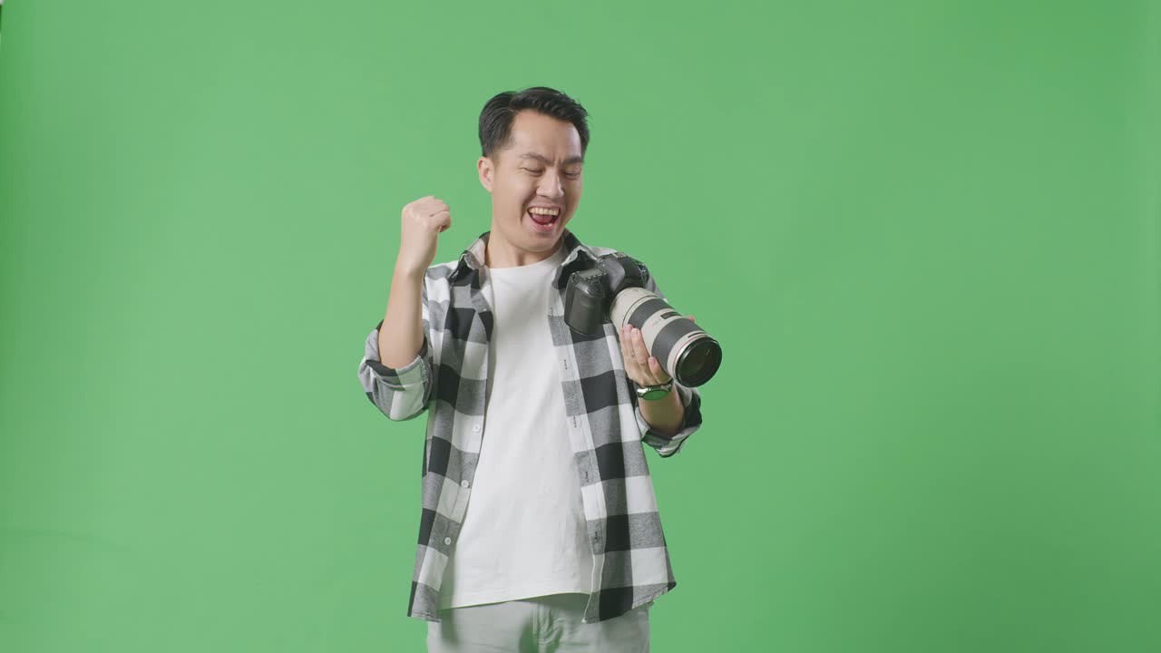 카메라에 있는 사진을 보고 있는 아시아인 사진작가, 그 다음에는 울부는 골과 춤을 추며 스튜디오의 녹색 스크린 배경에 서서 작업을 마치고 축하하고 있다.