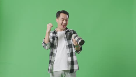 asian photographer looking at the pictures in the camera then screaming goal and dancing celebrating finishing his work while standing on green screen background in the studio