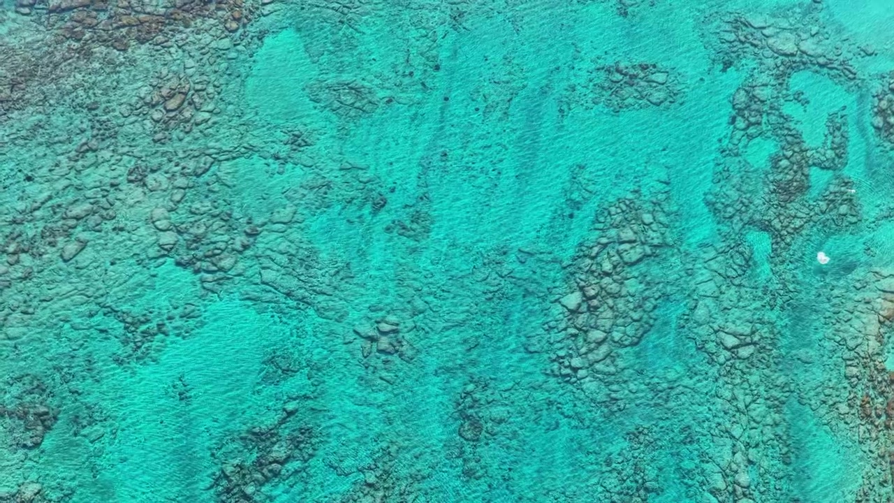 Luftaufnahme mit Drohne von oben von klarem türkisfarbenem Wasser über einem felsigen Riff in der flachen Lagune, Elafonissi, Griechenland